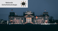 Bundestag bei Nacht. Auf dem Bild ist das Banner der Reihe "Nationale Sicherheitsstrategie" abgebildet.