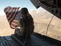 U.S. Marine Corps Capt. Kimberly Sonntag holds the American flag out the back of a CH-47 Chinook Helicopter as it moves to Operating Base Fenty, Dec. 24, 2017 (Foto: U.S. Department of Defense, Flickr, Public Domain).